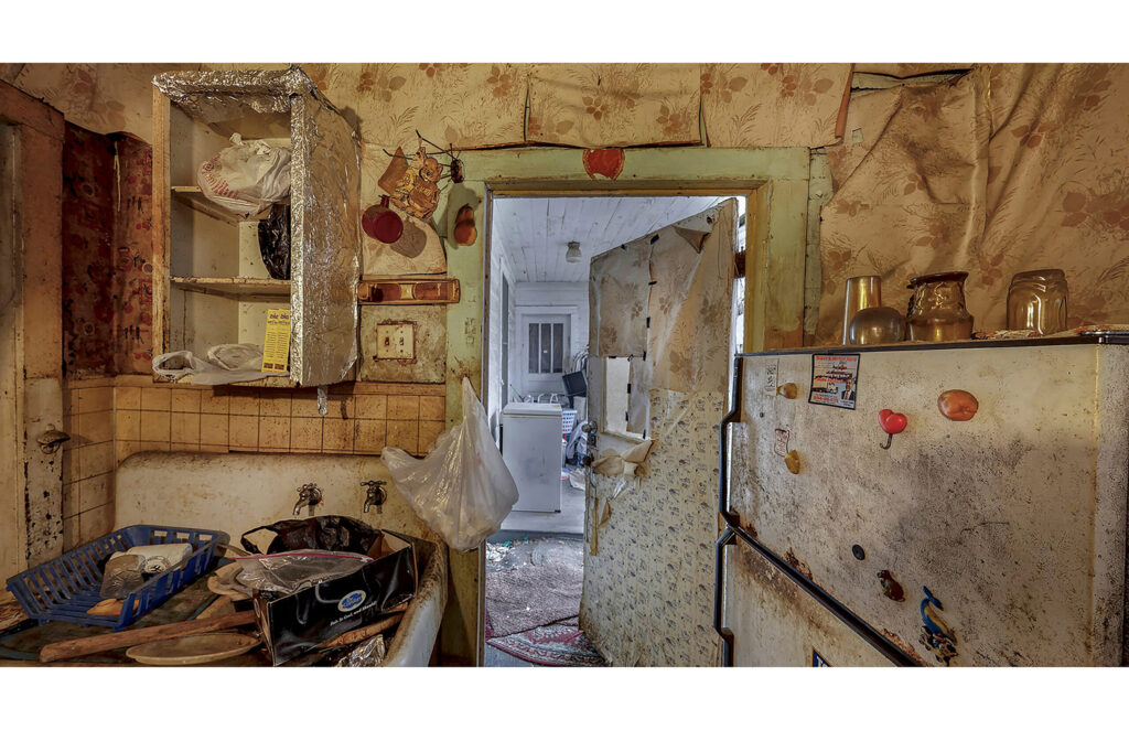 Worn kitchen with open doorway, aged cabinets, stove, and household items.