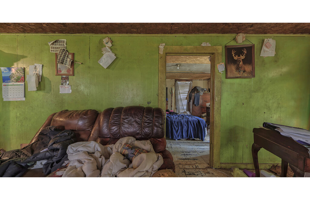 Green-walled room with worn sofa, bedding, open doorway, and personal items on the walls.