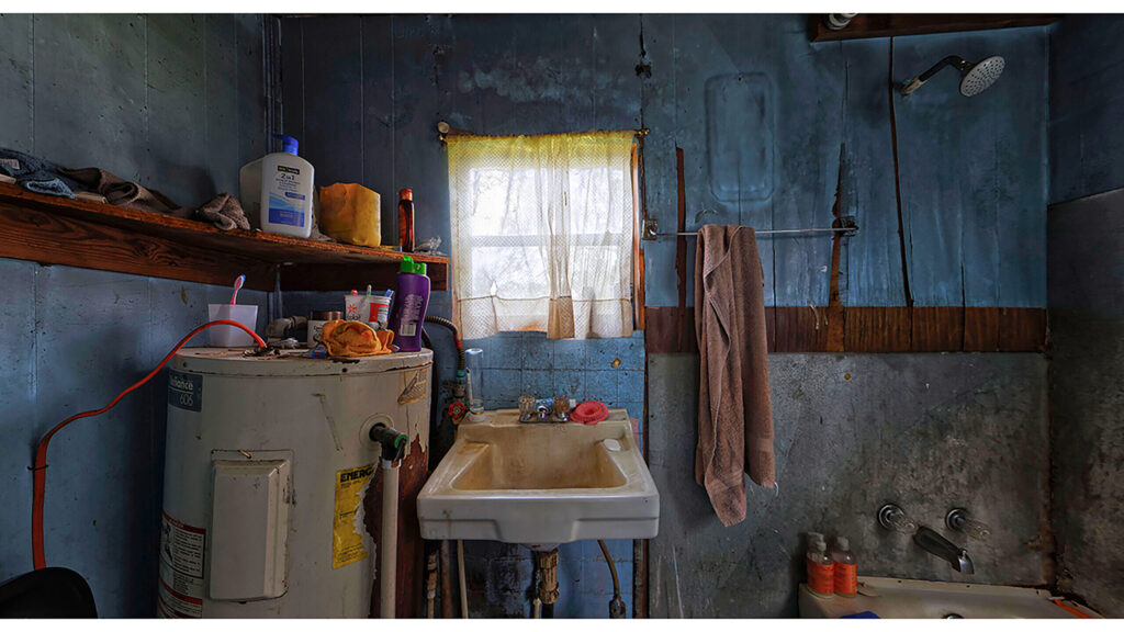 Blue bathroom with water heater, sink, curtained window, and exposed plumbing.