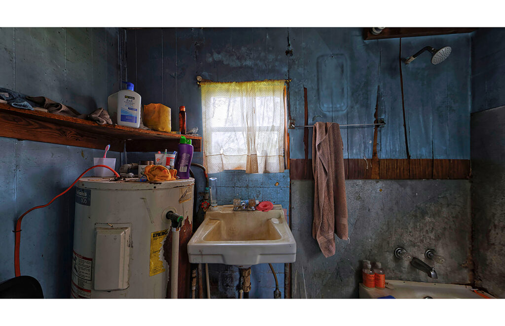 Blue-walled bathroom with sink, bathtub, window, shelving, and personal objects