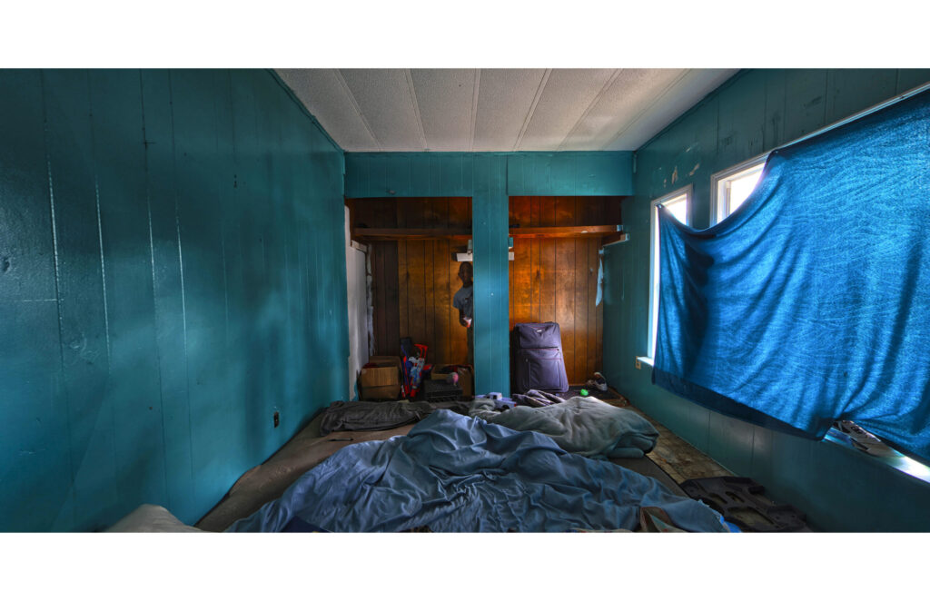 Blue-walled bedroom with unmade bed and fabric covering the windows.