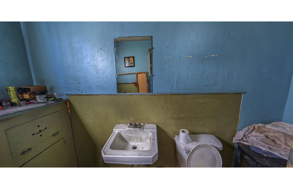 Blue-walled room with sink, toilet, dresser, and household items along the wall.