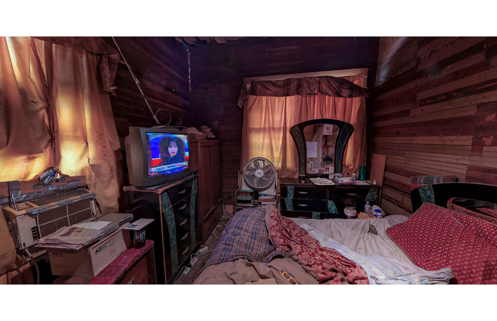 Green-walled room with worn sofa, bedding, open doorway, and personal items on the walls.