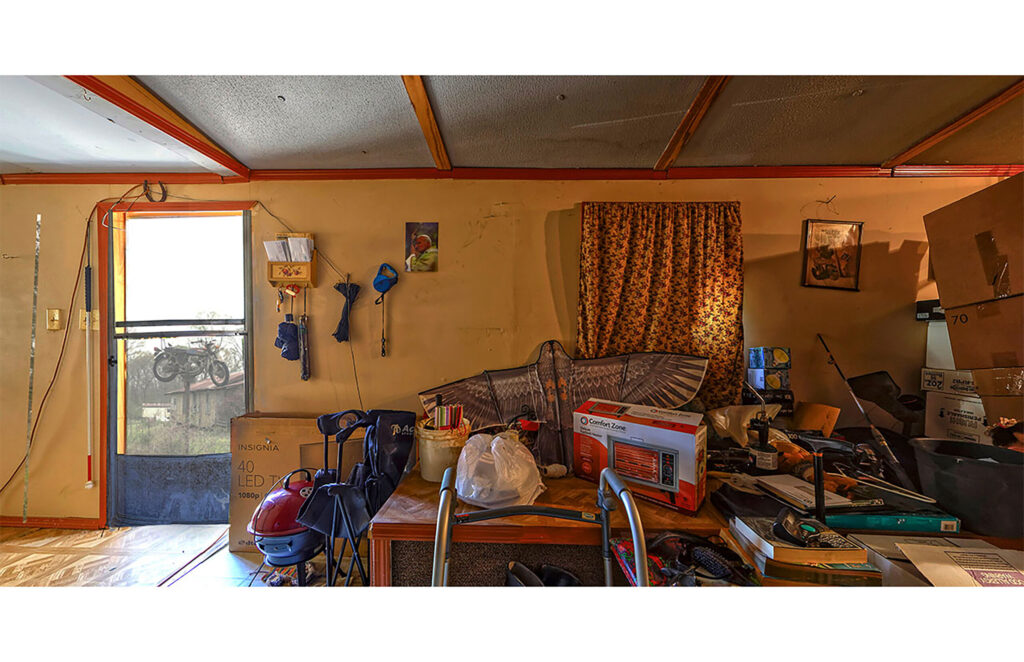 Cluttered living room with open doorway, stacked household belongings, and warm interior light.