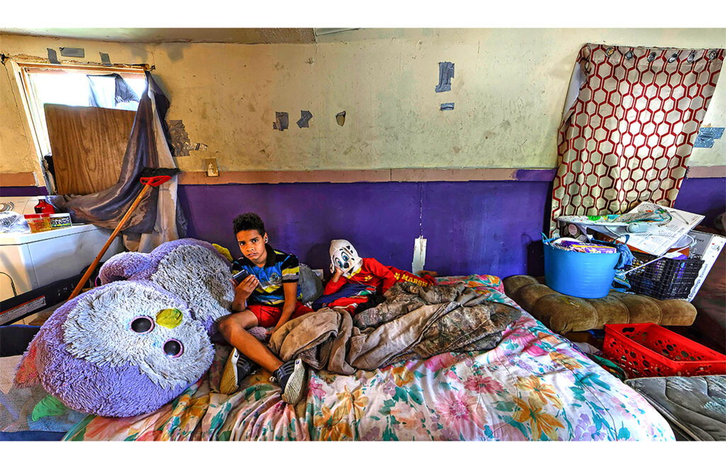 Child seated on a bed among colorful bedding, toys, and a large stuffed animal.