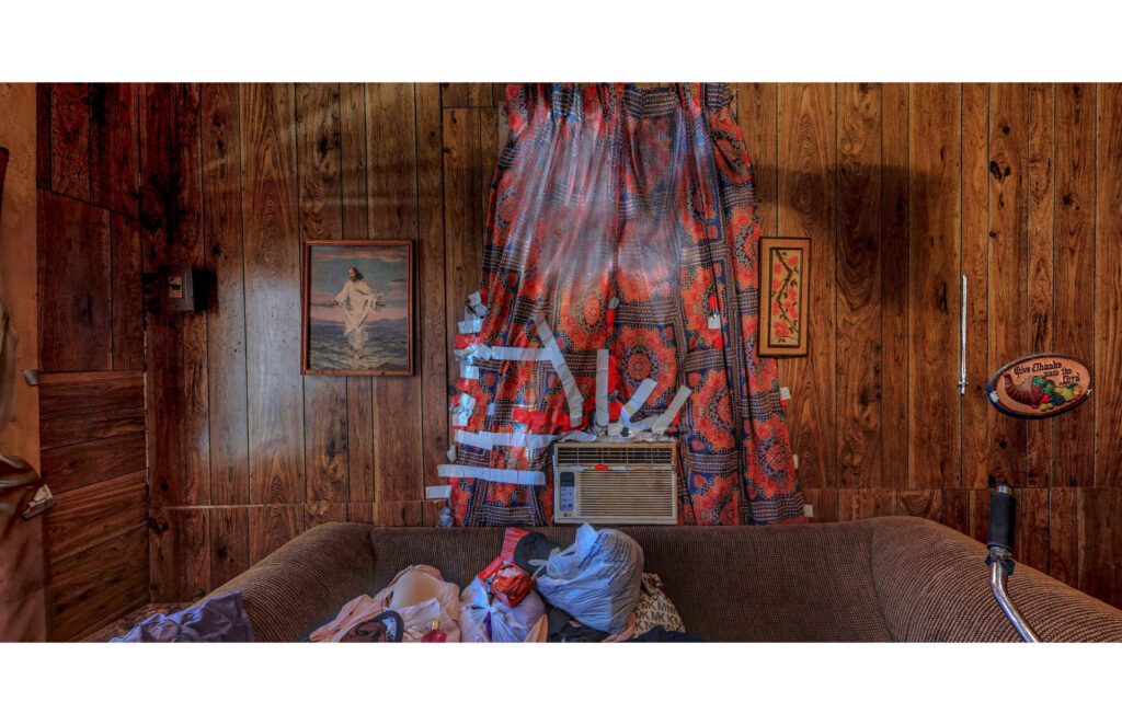 Wood-paneled room with sofa, hanging patterned fabric, framed pictures, and personal belongings.