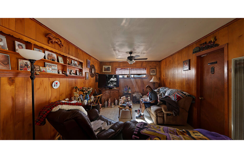 Long wood-paneled living room filled with furniture, shelves, and household belongings.